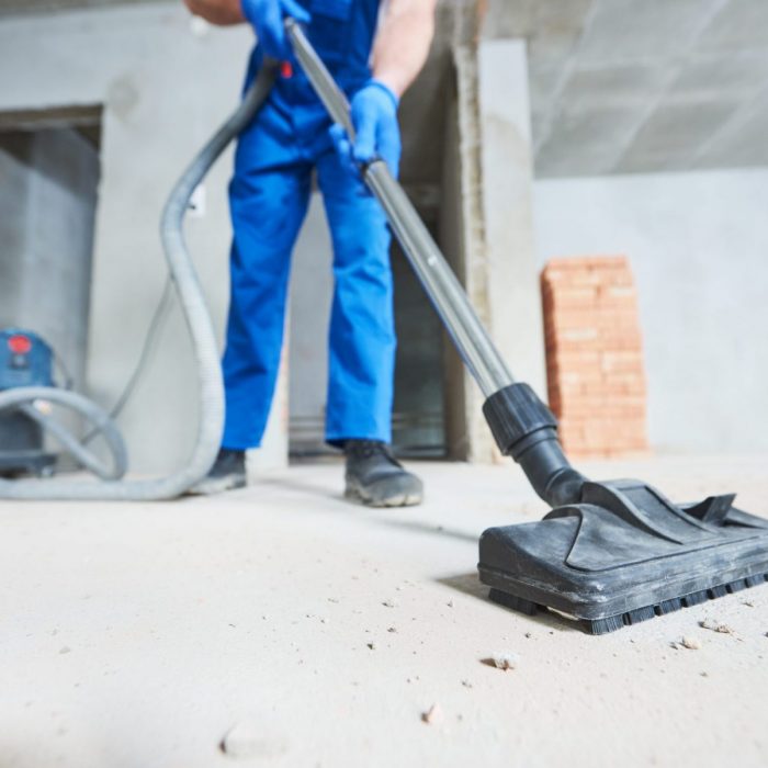 young woman cleaning and removing construction dust with vacuum cleaner after repair